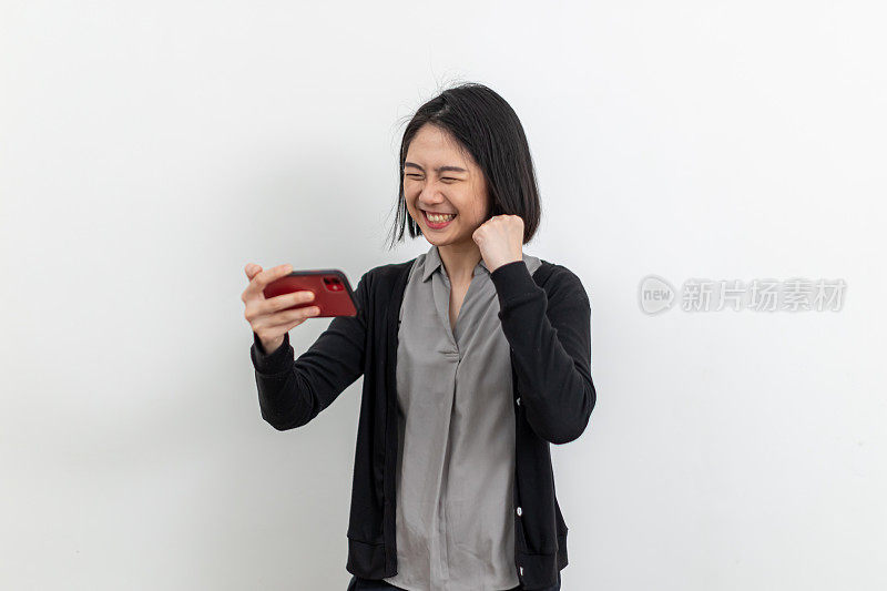 亚洲年轻女子拿着手机，脸上带着胜利的表情