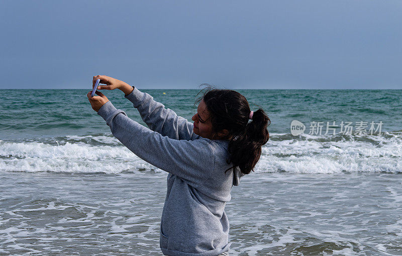 年轻女子在海边用手机拍照，留有复印空间