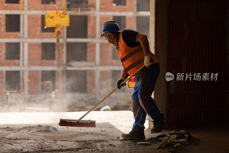敬业的建筑工人用扫帚清理工地上的灰尘