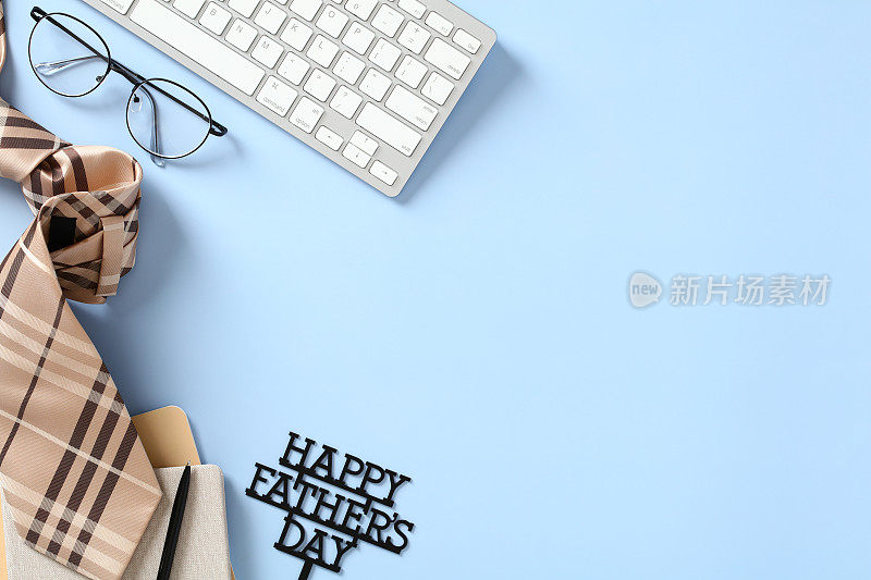 父亲节快乐贺卡设计。用键盘平铺构图，眼镜，文字父亲节快乐，蓝色桌子上的复古领带。
