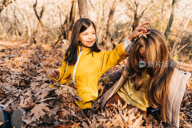 两个女孩坐在森林里的一堆枯叶上玩得很开心