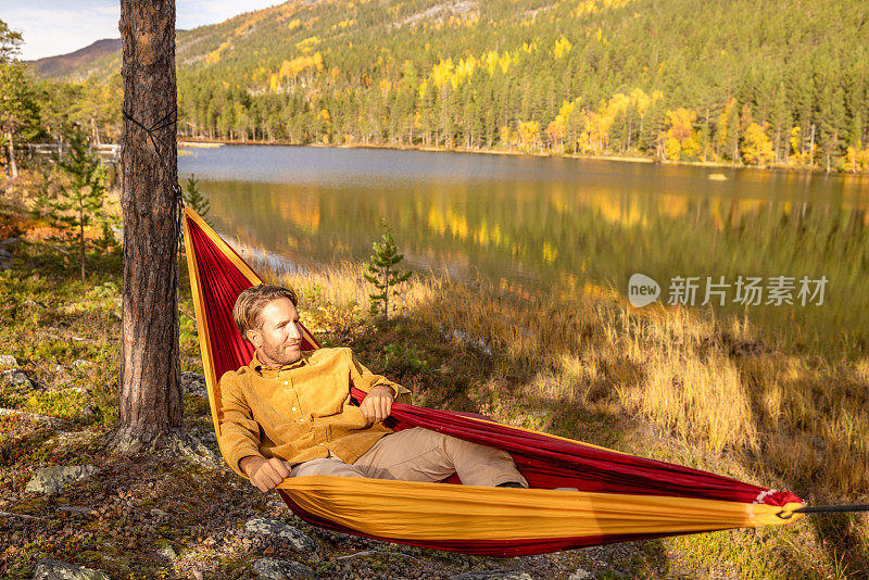 男人在湖边的吊床上休息，秋天的露营旅行