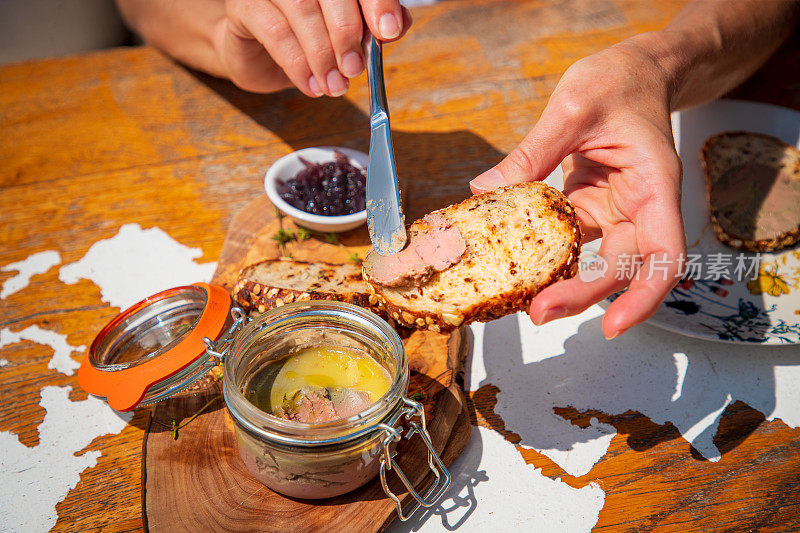 在木桌上用餐刀在面包片上涂鹅肉酱