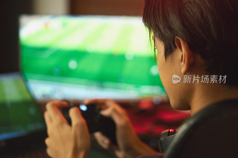 年轻的亚洲男子在家里的客厅边踢足球边直播多人在线游戏。