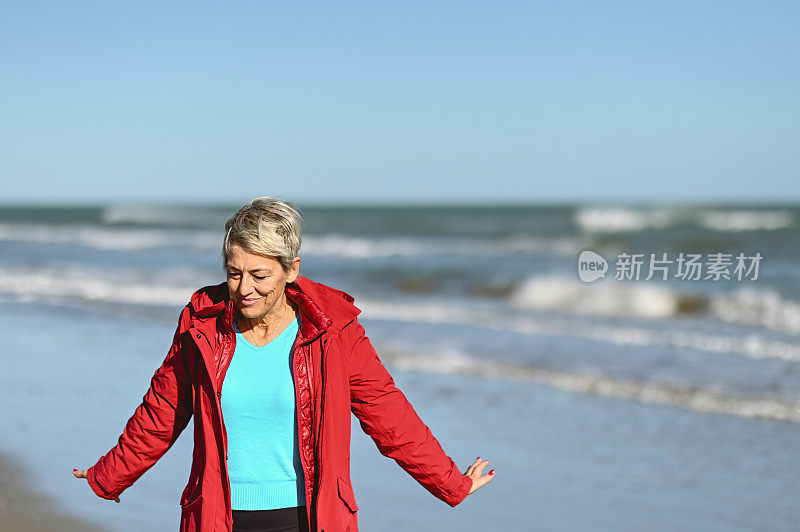 白发苍苍的女人站在狂风暴雨的海滩上。