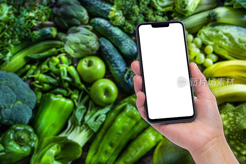 手持手机以绿色果蔬为背景，屏幕空白