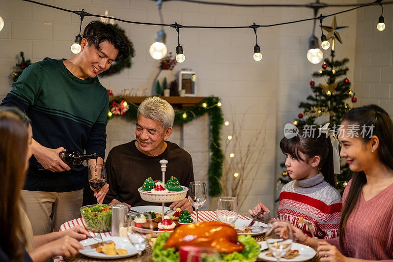 亚洲可爱的家庭在家里一起庆祝圣诞派对。迷人的父母和亲戚们在家里的餐桌上吃着感恩节大餐，庆祝圣诞前夜的节日。