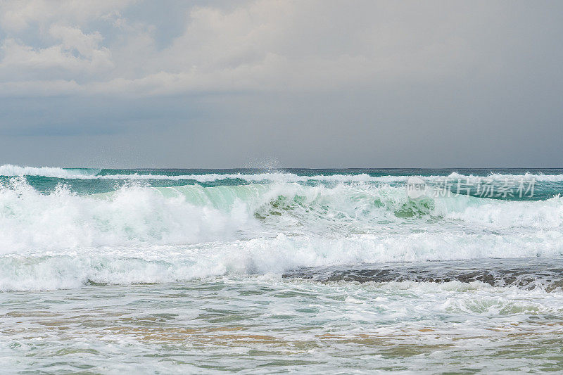 金色的沙滩:蓝绿色的海浪在多云的天空下撞击。巴厘岛，梦幻海滩。