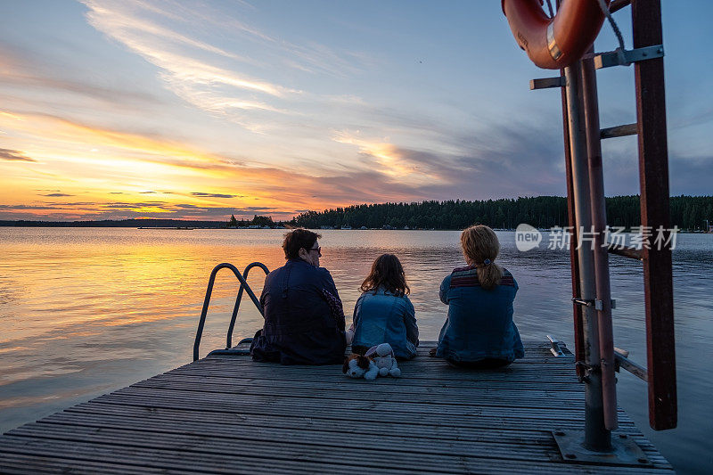 一个家庭，妇女和一个孩子在斯堪的纳维亚的一个湖上欣赏日落。地球上的夏天。