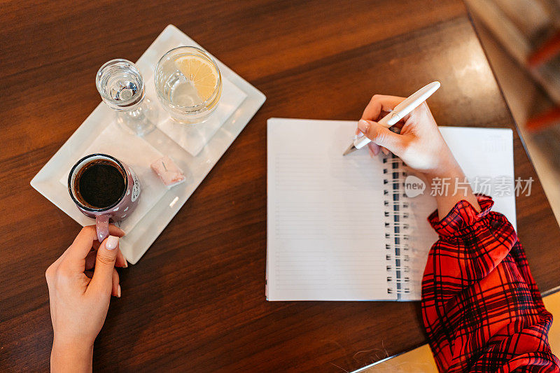 年轻女子一边喝咖啡，一边在咖啡馆里写笔记本