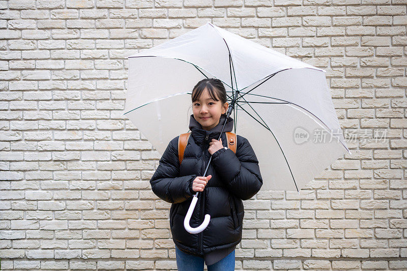 下雨天，日本一名小学生背着“随机书包”站在白色的墙上