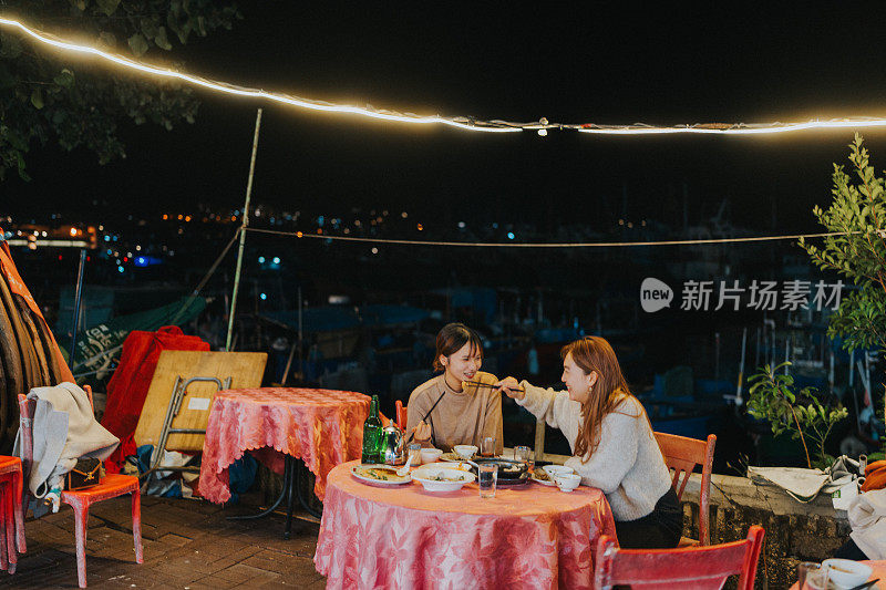 在香港长洲一个愉快的夜晚，两位年轻的亚洲女子正在大排洞享用晚餐