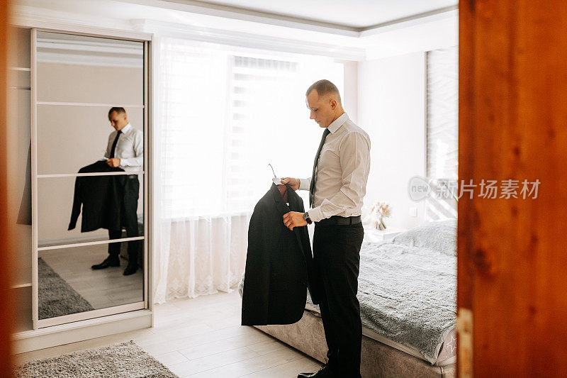 婚礼前，一名英俊的年轻男子穿上夹克，摆出新郎的姿势。新郎正在卧室里为婚礼做准备