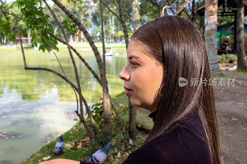 美丽的年轻女子在湖前的公园里望向远方