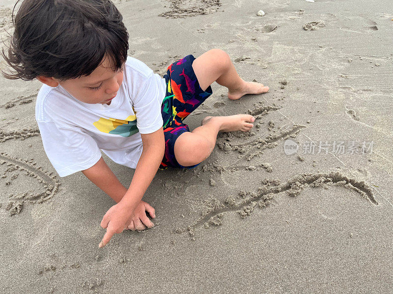 小男孩用手指在沙子上写字