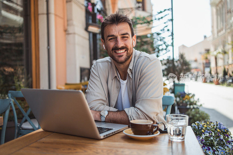 一个快乐的年轻人坐在咖啡馆花园享受美丽的早晨和早上的咖啡，用笔记本电脑打视频电话