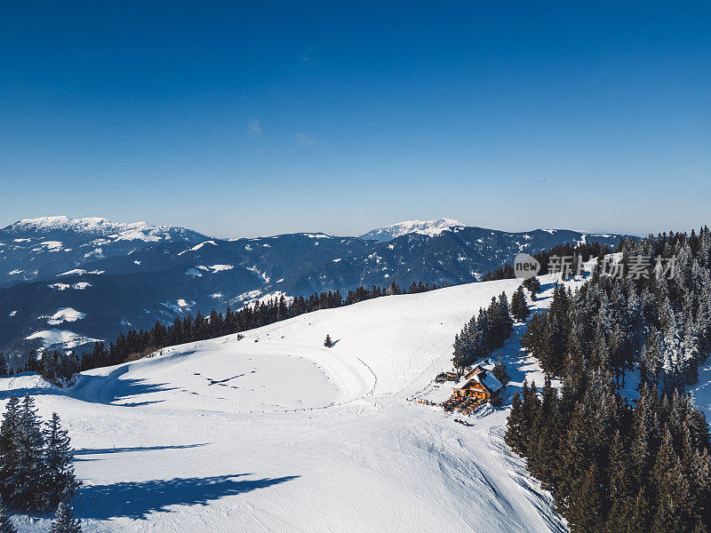 航拍的当地一个小滑雪胜地，有山间小屋、滑雪坡和结冰的湖。