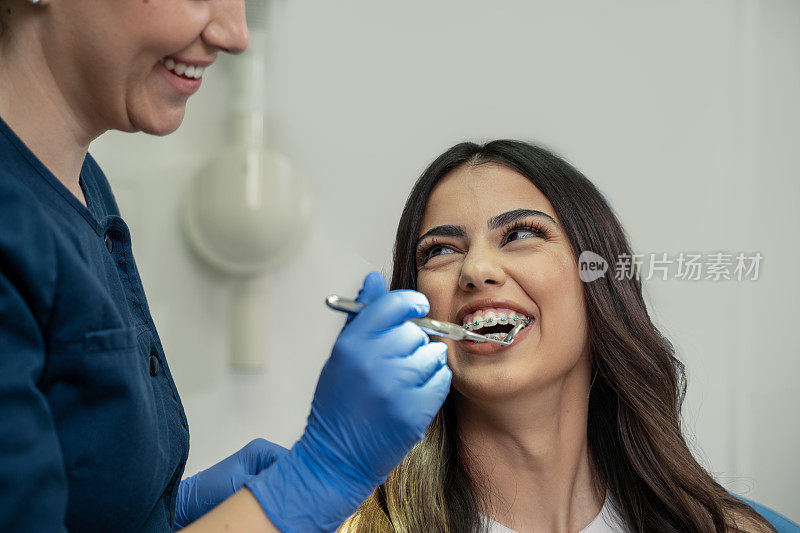 特写镜头，可爱的年轻女子戴着牙套微笑着，她的牙医正在给她做检查
