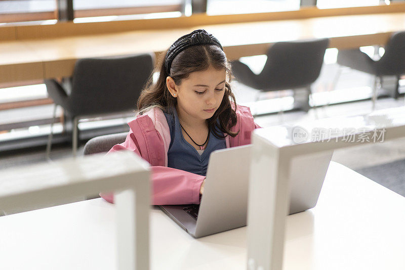 小女孩在图书馆用笔记本电脑学习