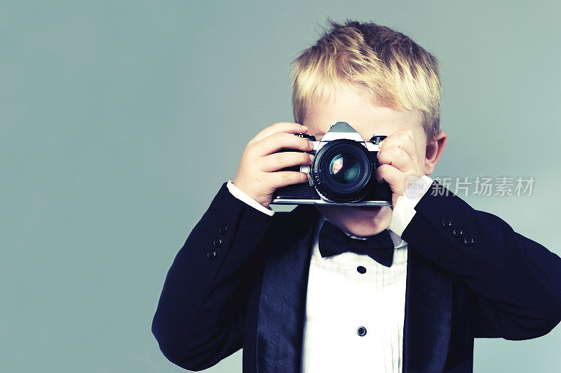穿着燕尾服的男孩用老式复古相机拍照
