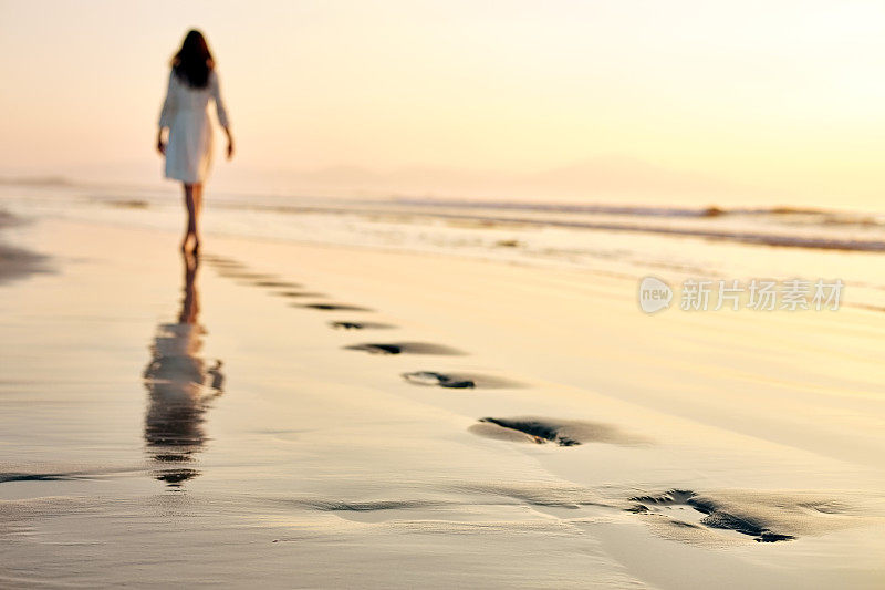 夕阳西下，女人在潮湿的沙滩上留下脚印
