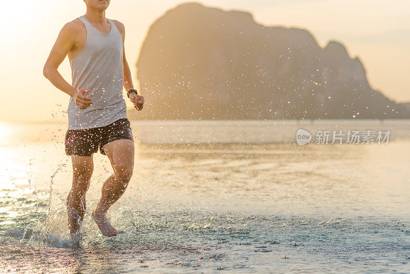 年轻的亚洲男子在海滩上奔跑，夕阳为背景