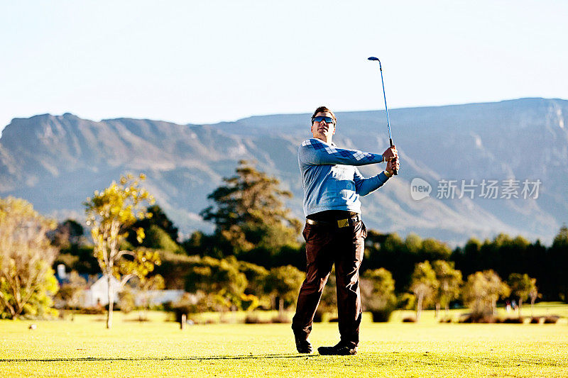 年轻的高尔夫球手在美丽的山脉背景下开球