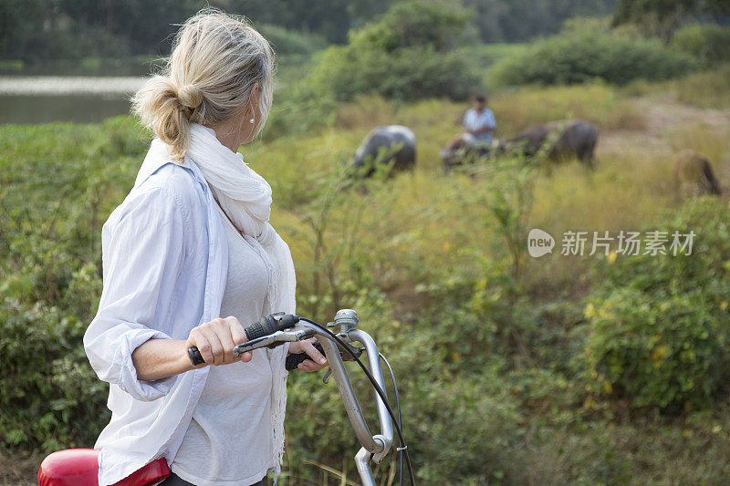 一个女人推着自行车经过河边的水牛