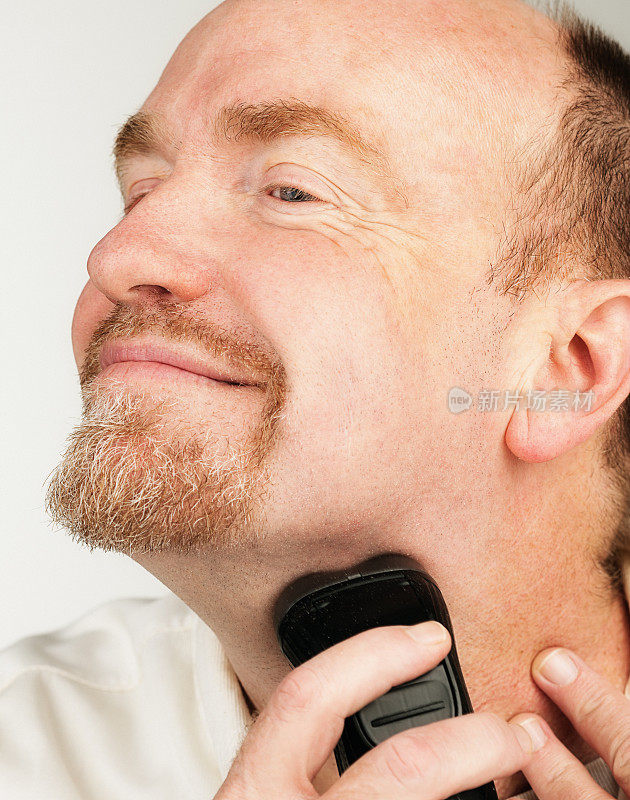 用电动剃须刀刮胡子的男人开心地笑着