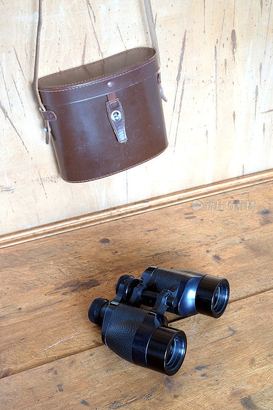老式棱镜黑色双筒望远镜和棕色皮箱在墙上