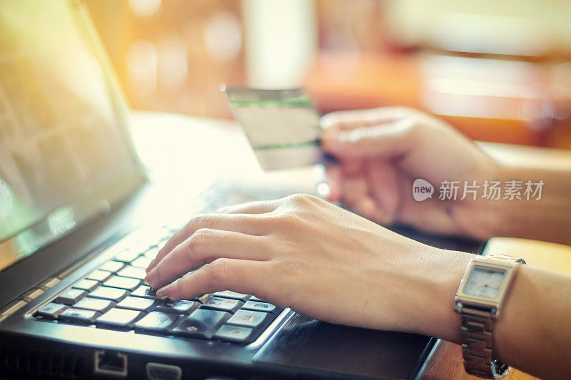 使用笔记本电脑和信用卡在网上购物的亚洲女性，选择性地关注手，柔和的焦点和复古色调
