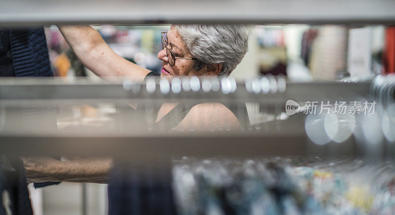这位满头银发、活跃的65岁老妇人正在一家服装零售店购物