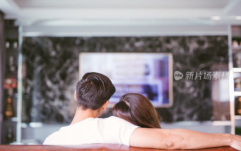 后视图的夫妇看电视在客厅拥抱