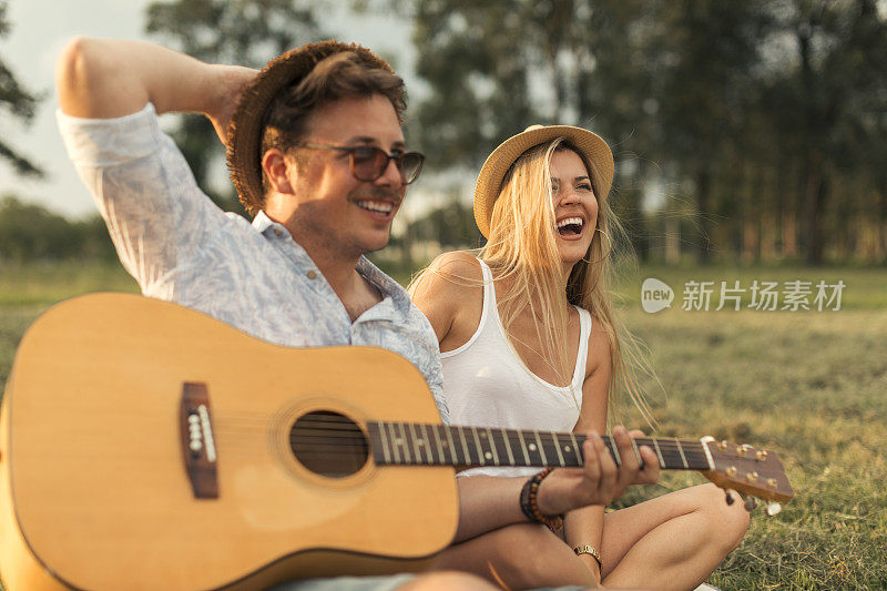 一对年轻情侣坐在草地上，手里拿着吉他