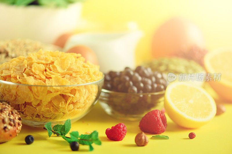 谷类玉米，什锦麦片，牛奶，浆果，橙汁，酸奶，煮鸡蛋，坚果，水果，香蕉，桃子早餐在黄色的背景。副本的空间。纯素和素食的概念。
