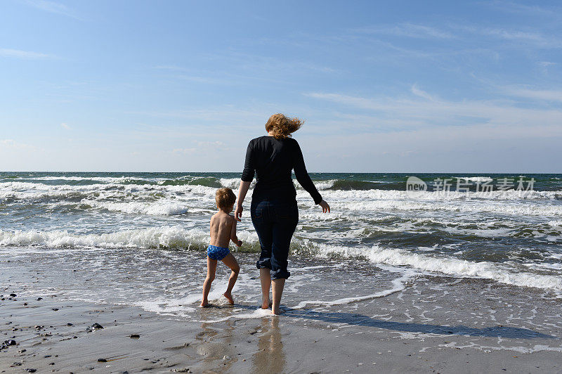 妈妈和儿子在海滩上。一个快乐的母亲和儿子在海滩上玩的后视图。