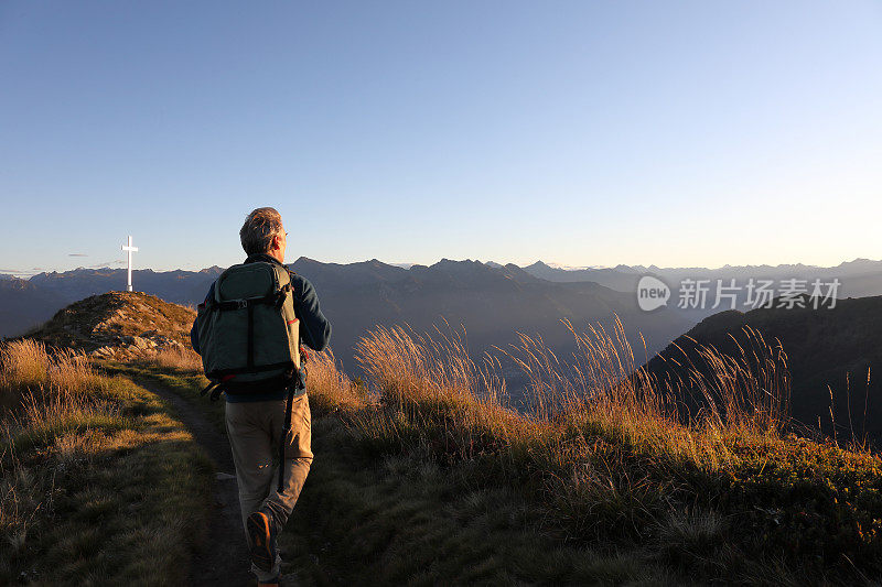 日出时，人们沿着长满草的山脊徒步旅行