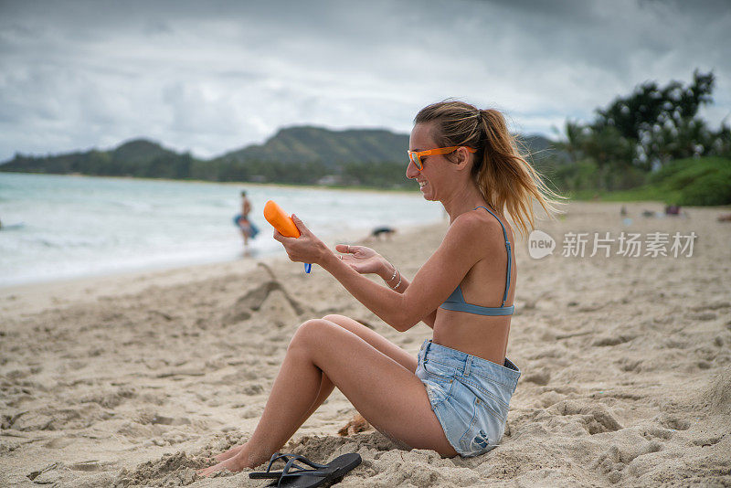 夏日——年轻女子在海滩上涂抹防晒霜，保护皮肤