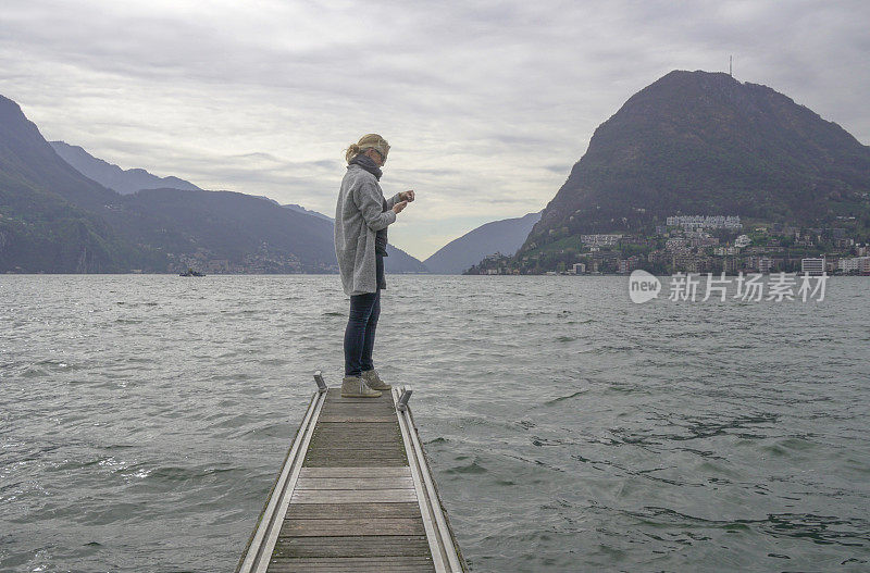 成熟的女人站在湖边的码头上用手机