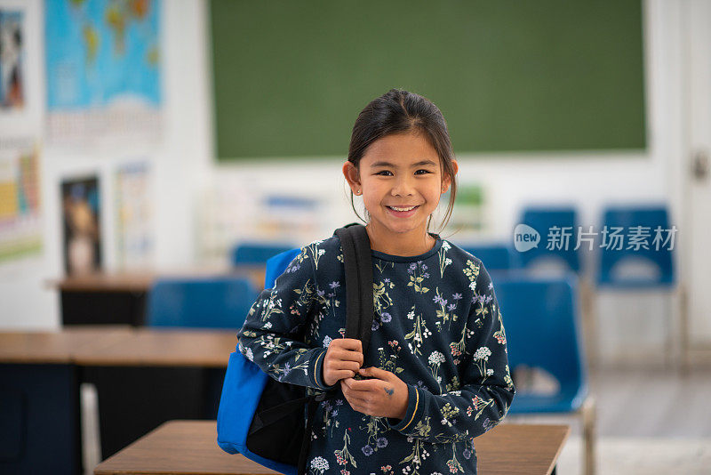 亚洲小学学生倚在书桌上，她的背包库存照片