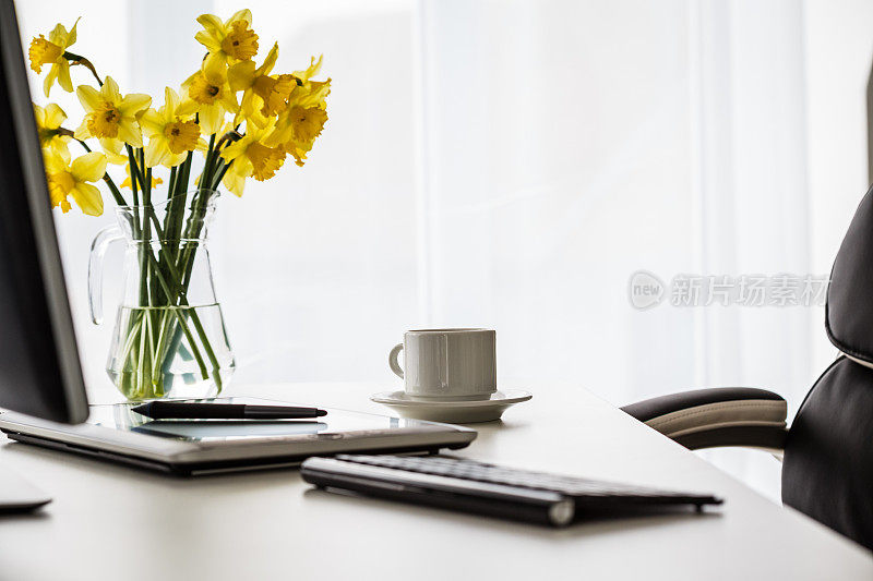 一张整洁的办公桌上放着一束黄色的水仙花，给人一种鲜艳的感觉