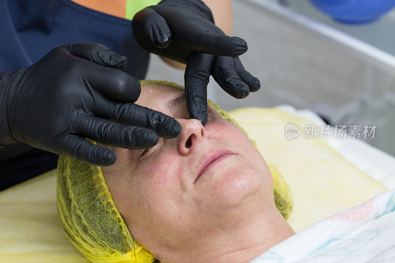 在开始化学脱皮程序之前，美容师的手按摩一个女人的脸。