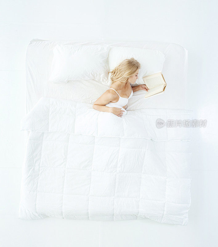 白人年轻女性睡在白色的背景在卧室穿着内衣和拿着书