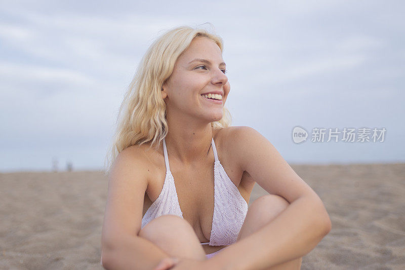 在海滩上，一个年轻女子双手捂着头微笑着