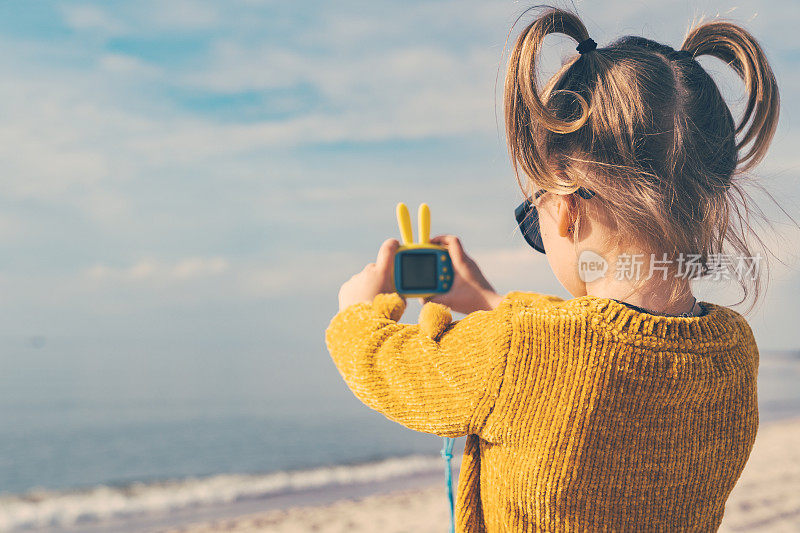 一个扎着有趣马尾辫的小女孩正在拍大海的照片。