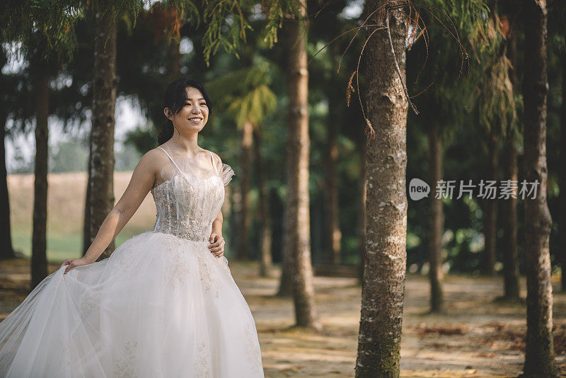 年轻的亚洲华人新娘穿着白色婚纱在公园摆姿势