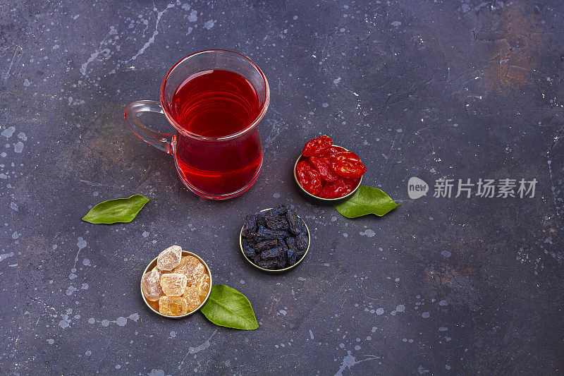 土耳其茶杯(armudu)中红茶(roibos，木槿，karkade)与山茱萸，葡萄干，糖在深色的背景上。草药，维生素，治疗感冒和流感的排毒茶。文本复制空间