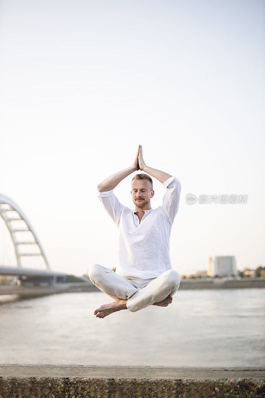 年轻美丽的男子在半空中沉思的肖像，漂浮在户外地面上，坐在莲花姿势，莲花身