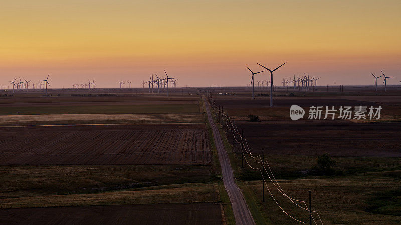 日出前在堪萨斯州的农田和风力涡轮机之间的长直路
