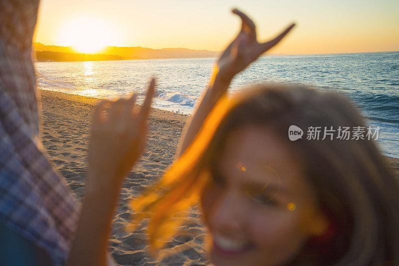 日落或日出时，和朋友在海滩上跳舞的女人。